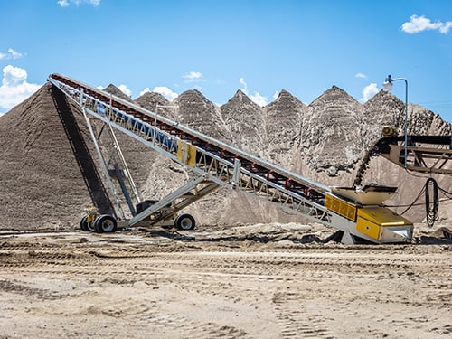 Portable Radial Stacker in operation stockpiling large sand pile fed by secondary conveyor